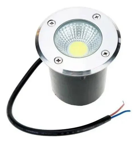 A round, recessed Farol de suelo LED 6w Negro circular de piso ip67-RGB, with a metal rim and black cylindrical body. Two exposed wires (red and blue) extend from the cable. Exterior ground light with remote control included.